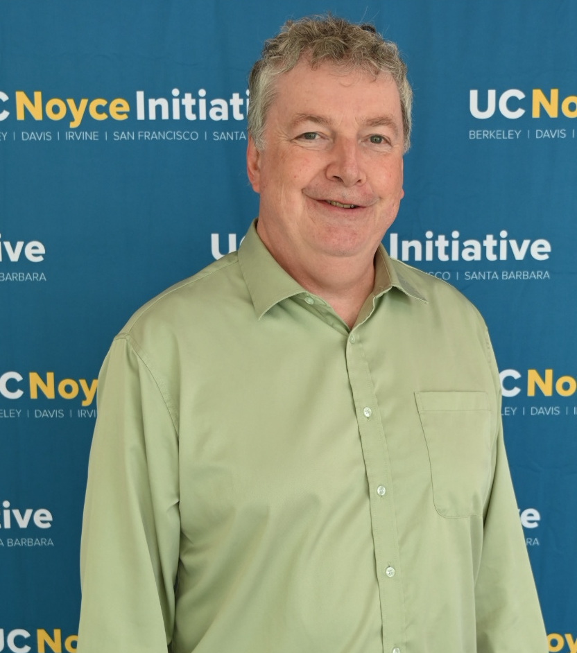 man in green shirt in front of UC Noyce Initiative backdrop.