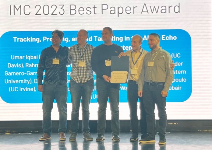 Researchers standing on stage with certificate for winning best paper for “Tracking, Profiling, and Ad Targeting in the Alexa Echo Smart Speaker Ecosystem”.