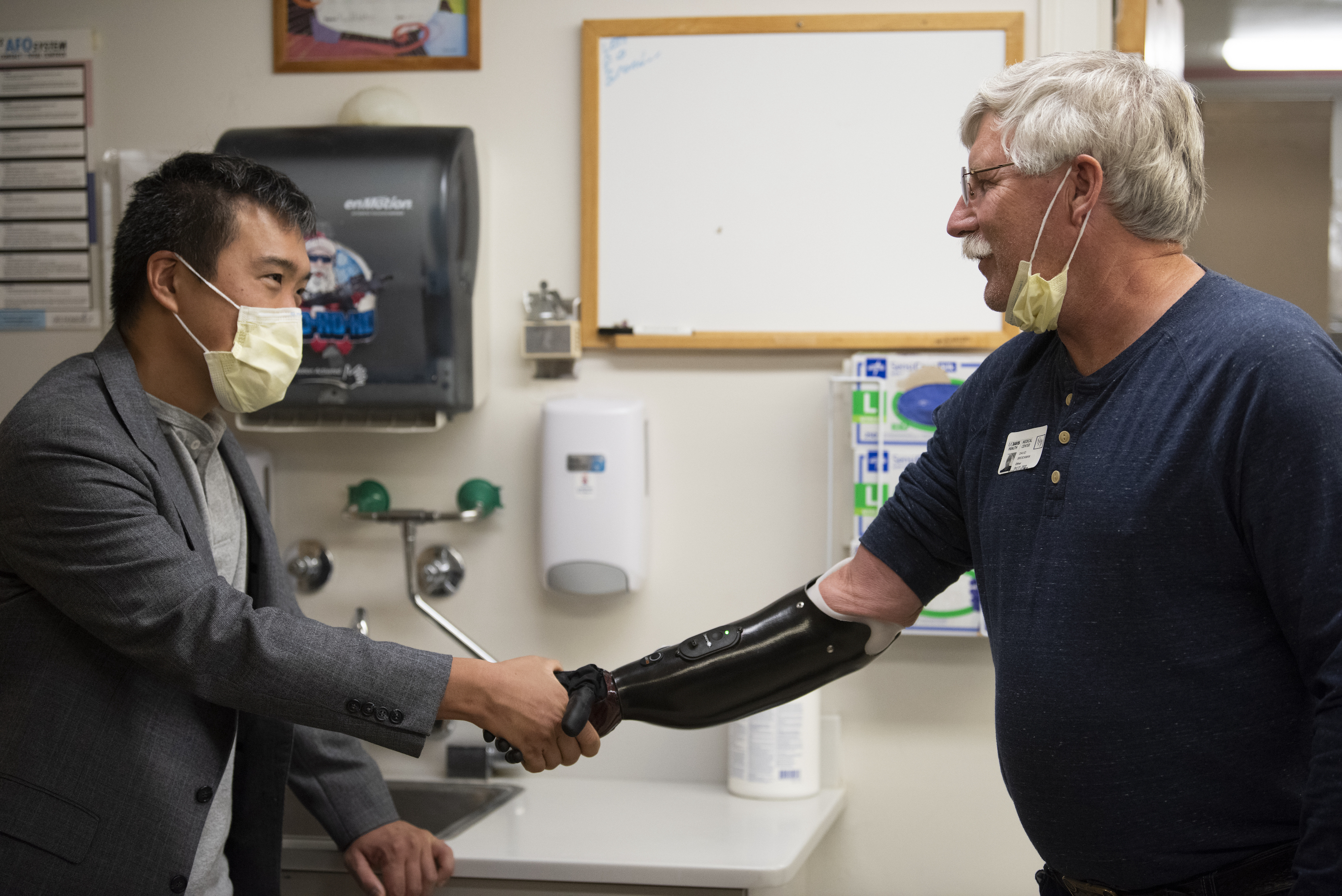 a man in a coat shakes the hand of a man wearing a prosthetic arm.