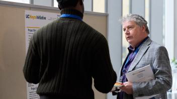 two men talk at a poster