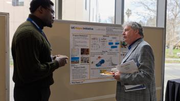 two men talk at poster