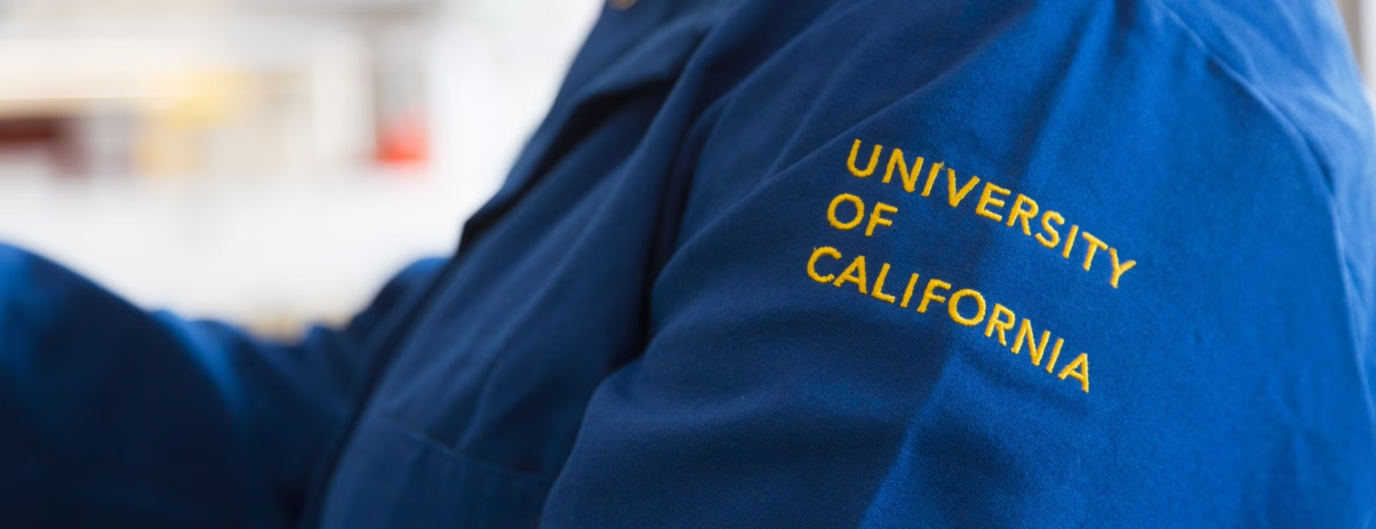 close up of arm in blue lab coat that says university of california