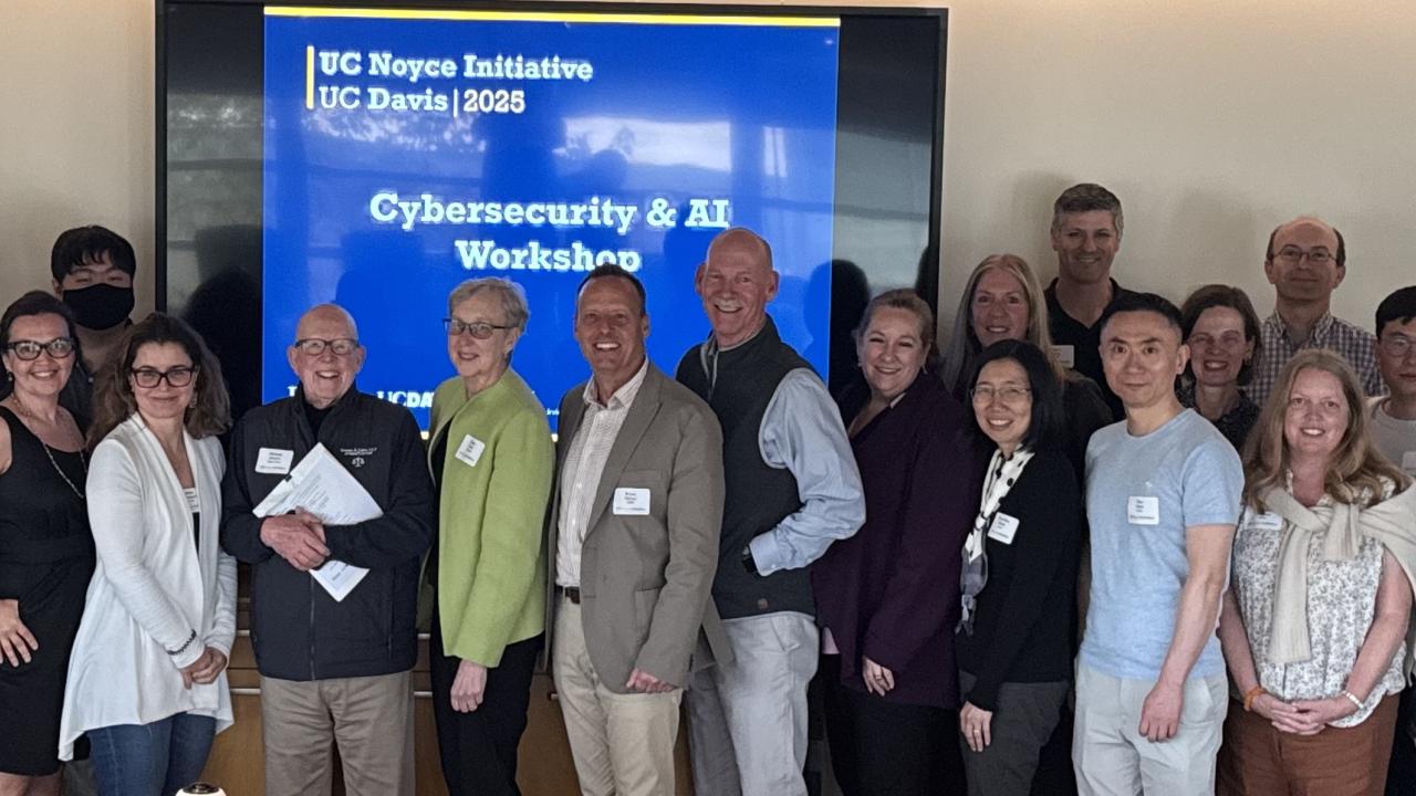 group of people stand in conference room with UC Noyce Cybersecurity Workshop slide in the background
