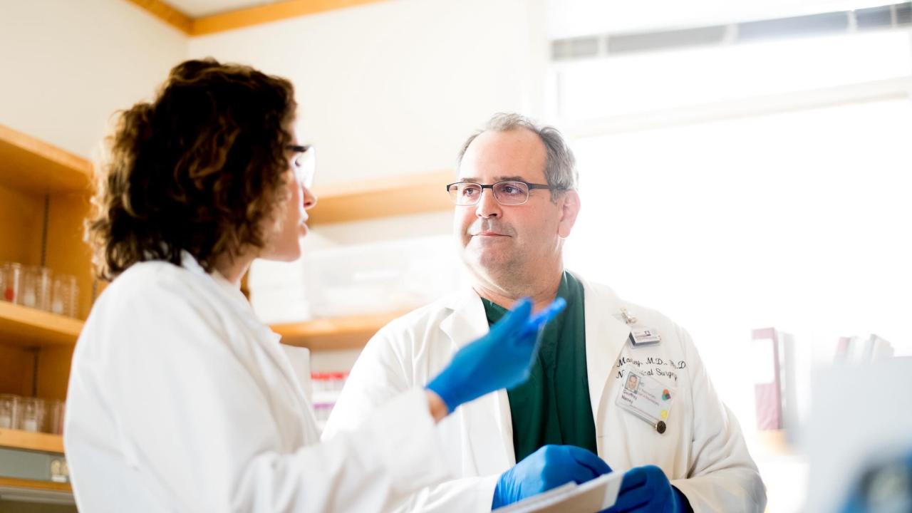 Geoffrey Manley, M.D., Ph.D. Professor Neurosurgery UC San Francisco talks with female coworker in lab.