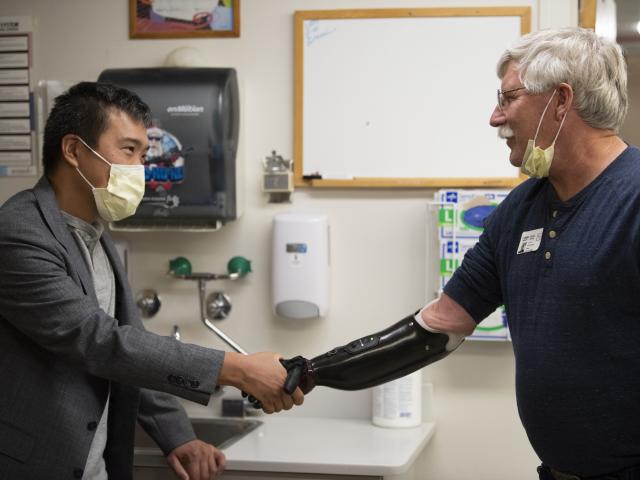 a man in a coat shakes the hand of a man wearing a prosthetic arm.