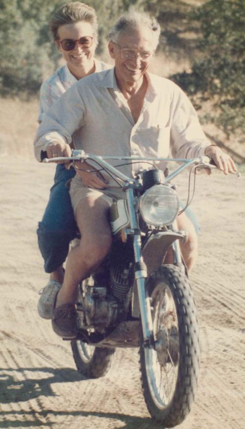 Woman wearing sunglasses and man wearing glasses smile as they ride a dirt bike