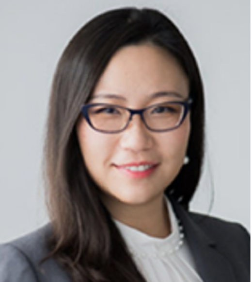 Portrait of Jing Meghan Shan, an Asian woman with dark hair that is swept over her shoulder one one side. She is wearing dark rimmed glasses, a white blouse and a dark grey sports coat.