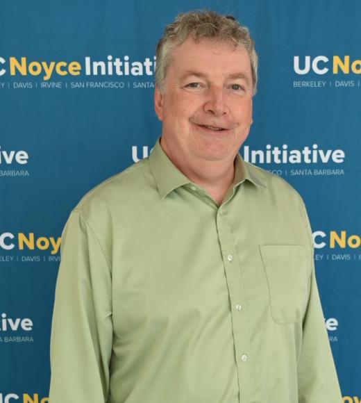 man in green shirt in front of UC Noyce Initiative backdrop.