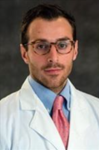 Doctor Julien Cobert wearing glasses a white medical coat, blue shirt and pink tie