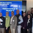 group of people stand in conference room with UC Noyce Cybersecurity Workshop slide in the background