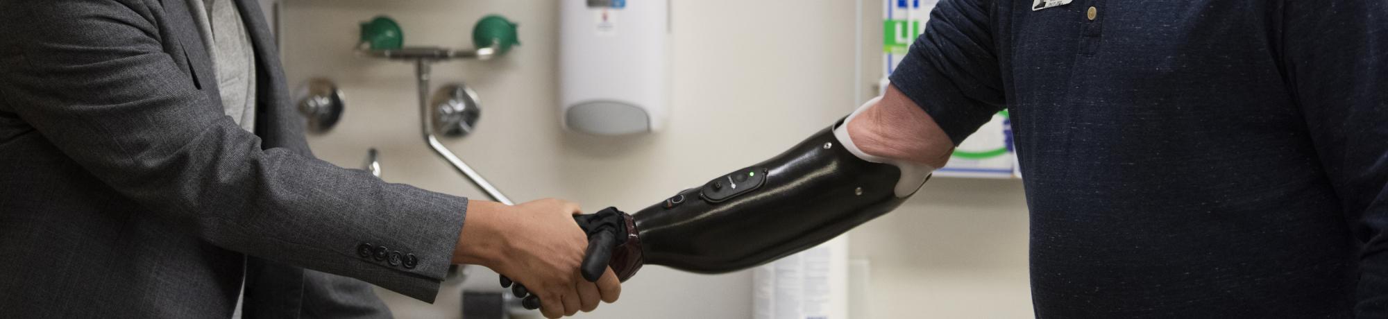a man in a coat shakes the hand of a man wearing a prosthetic arm.